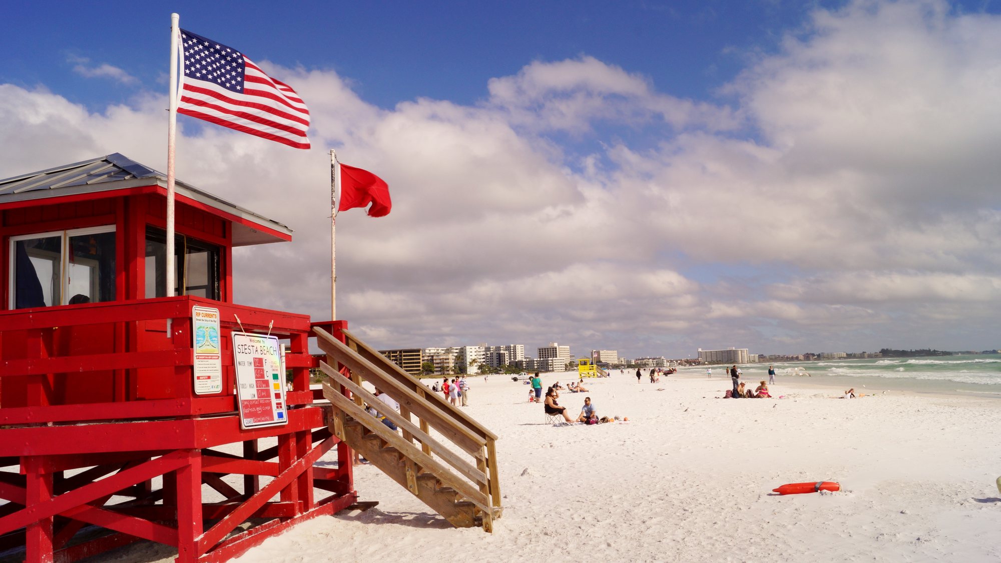Red lifeguard stand with Welcome to Siesta Beach sign on white sand